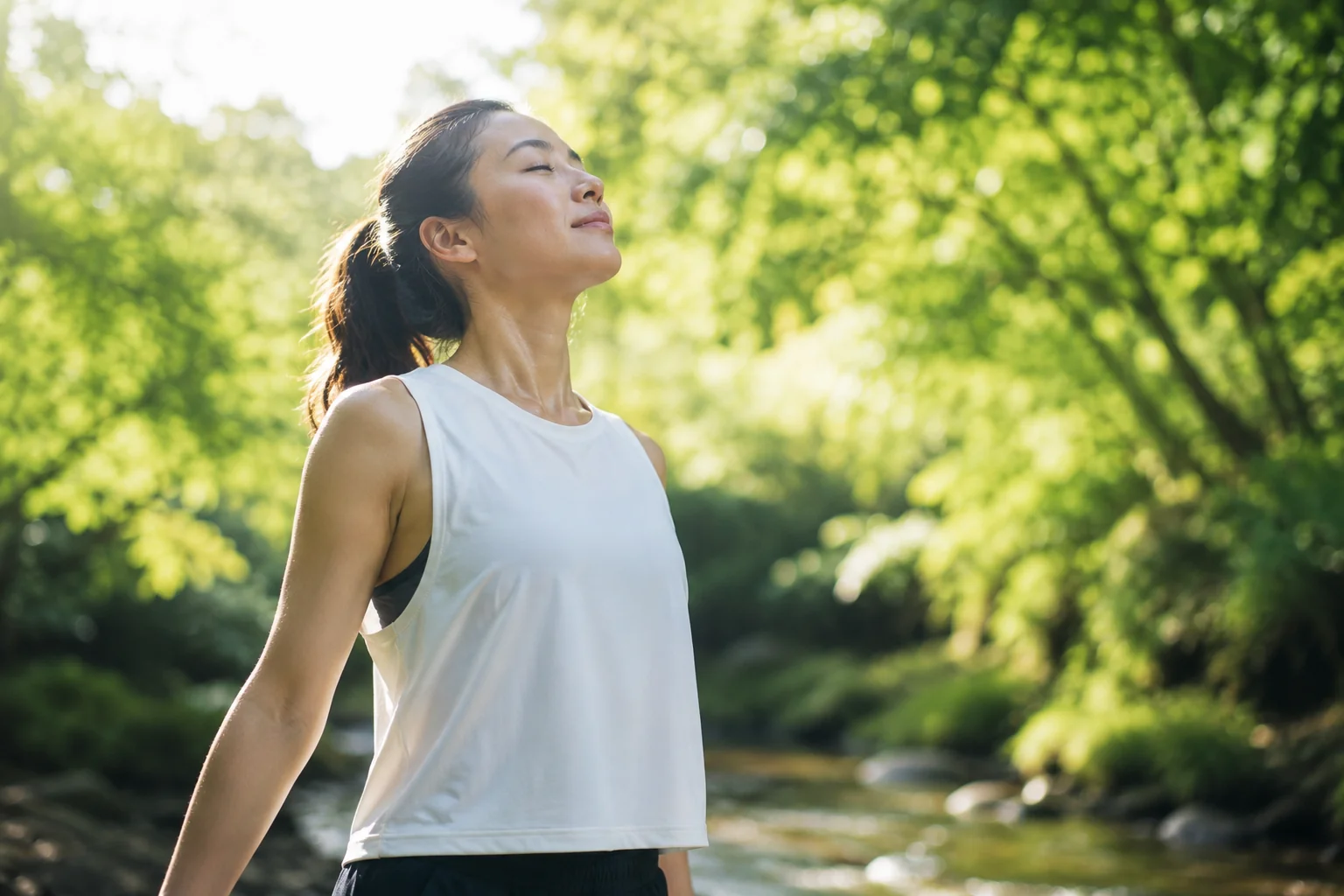 木漏れ日の差す水辺で、目を閉じて深く息を吸い込むランナー